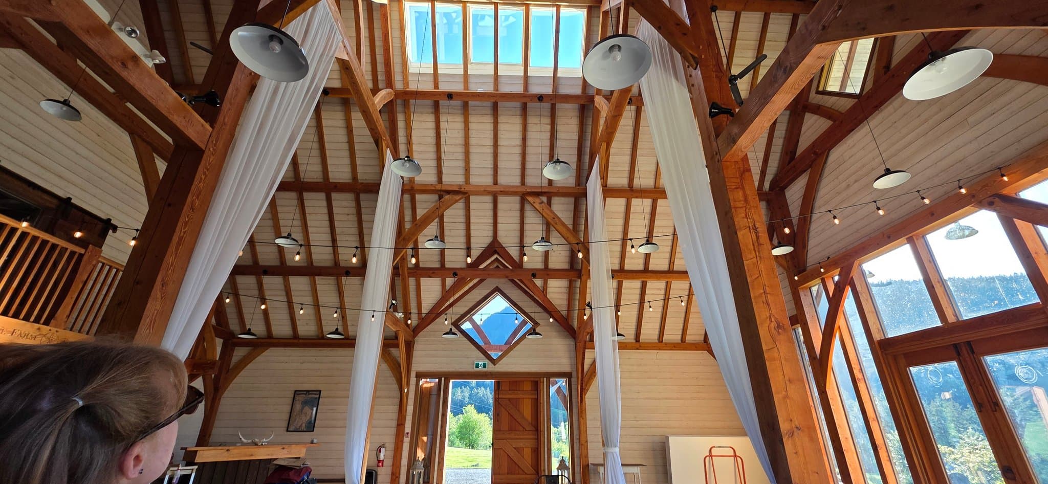 Looking up at the barn's timber beams, drapes and string lights